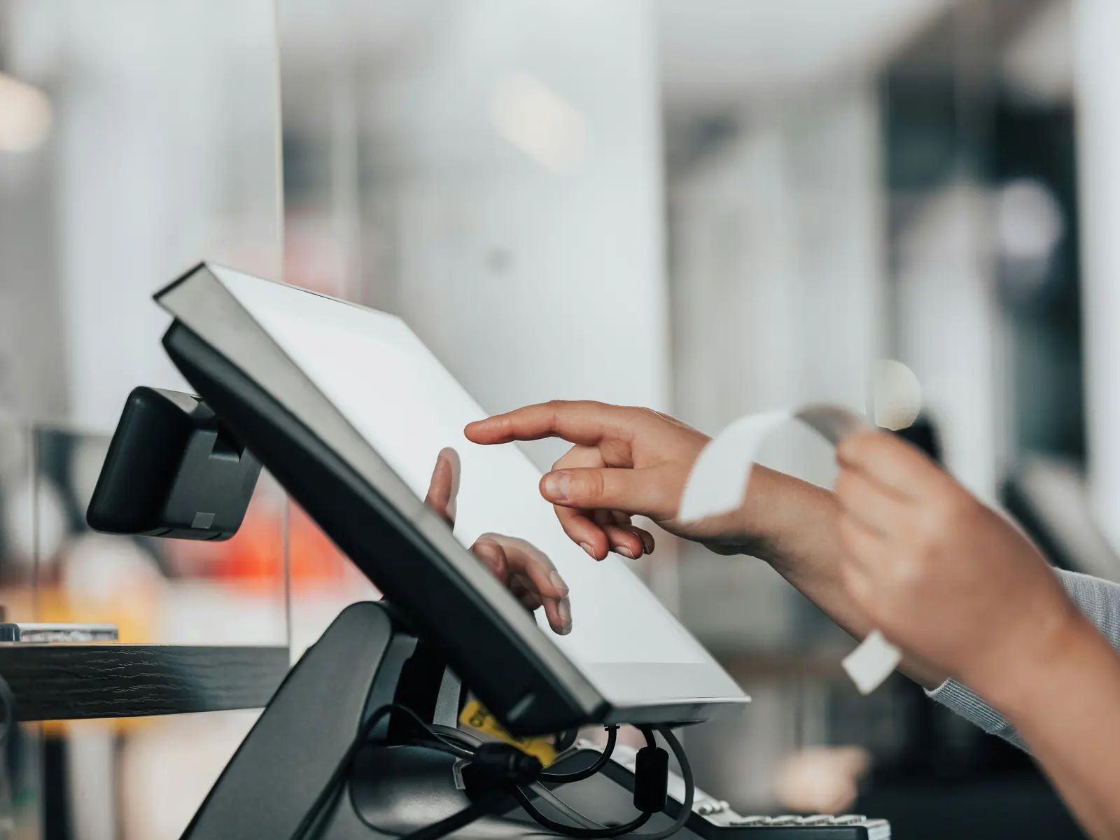 A cashier holds a printed receipt while ringing up a sale on a touchscreen point-of-sale terminal