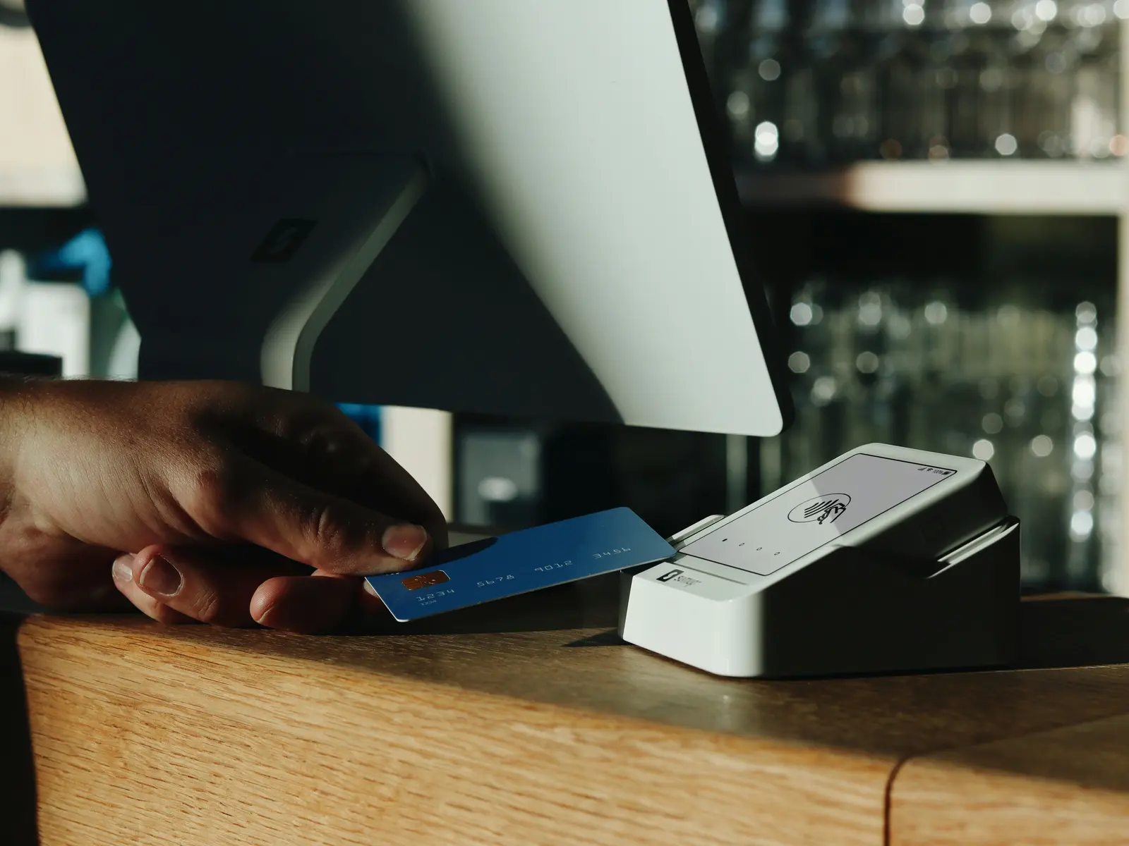 A customer taps a chip card on a countertop payment terminal at a wooden shop counter