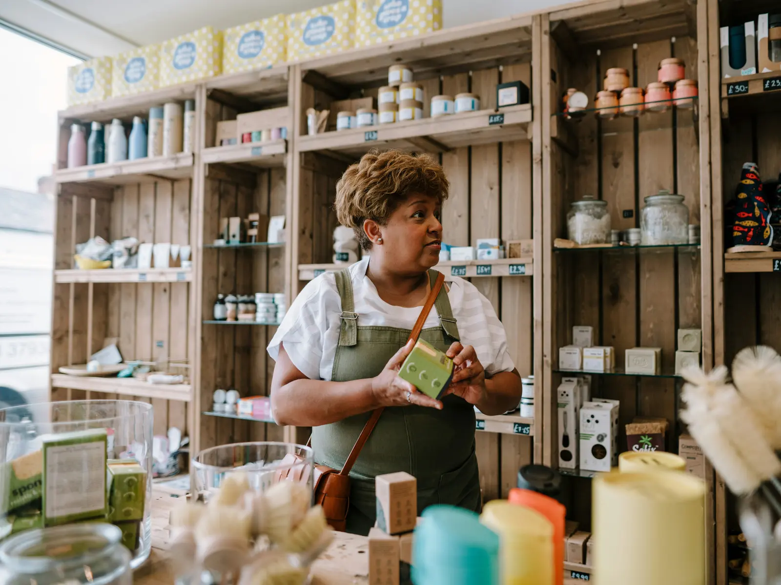 The owner of a small homewares shop holds a product in front of wooden shelves